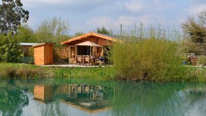 Eine Holzhütte mit Essbereich und einem kleinen Geräteschuppen, gelegen an einem ruhigen See mit Spiegelungen.