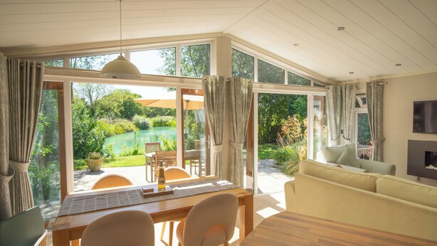 Amplia habitación con un ventanal que ofrece vistas a un jardín y piscina. Hay una mesa de comedor con sillas, un sofá y un televisor montado en la pared.