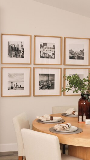 Comedor con una mesa redonda, seis fotografías en blanco y negro enmarcadas en la pared y una planta en maceta sobre la mesa.
