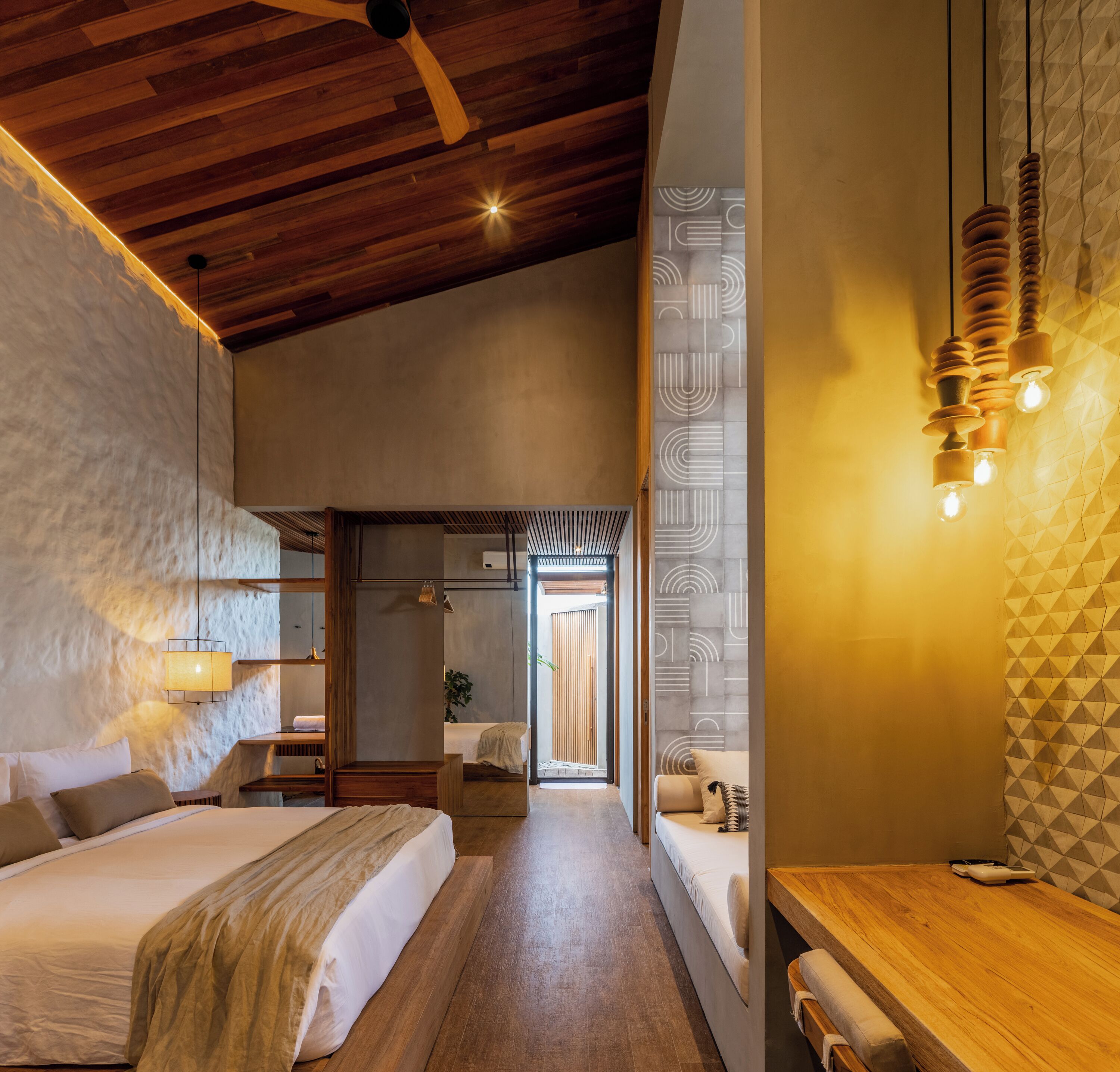 Une chambre d’hôtel moderne avec un plafond en bois, un grand lit, un bureau en bois et un mur orné d’un motif géométrique.