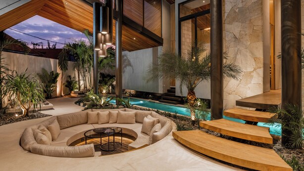 A modern indoor pool area with a curved seating area, stone walls, and a wooden ceiling.
