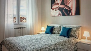 Ein Schlafzimmer mit einem geblümten Bettüberwurf, zwei Kissen, einem Nachttisch mit Lampe und einem großen Gemälde an der Wand.