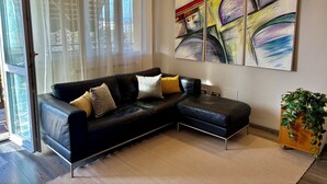 Ein modernes Wohnzimmer mit einem schwarzen Leder-Modulsofa, einem großen abstrakten Gemälde und einem Holz-Pflanzentisch.