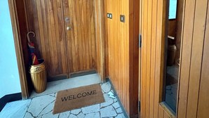 Eine Holztür mit Fußmatte, ein kleiner Podeststufen zum Eingang und eine Holzwand mit Fenster.