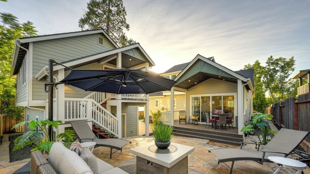 A patio area with a covered seating area, a stone floor, and a staircase leading to an upper level.