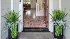 A front entrance with a wooden floor, a red carpet, and two potted plants.