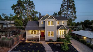 A two-story house with a front porch, a red door, and a landscaped front yard with stone pathways.