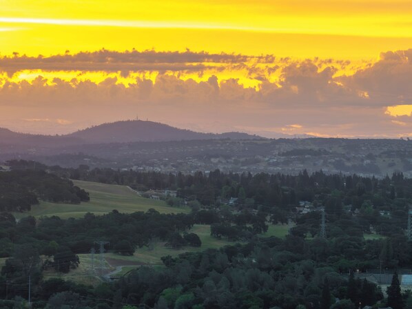 Vista panorámica de un paisaje con una colina al fondo, un valle con casas dispersas y un cielo despejado.