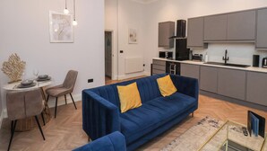 A modern apartment with a blue sofa, a dining area, and a kitchen with grey cabinets. - The Salisbury Apartment 103 (Scarborough)