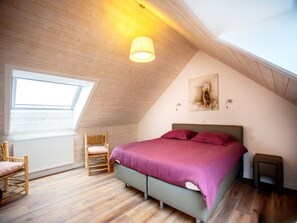 A bedroom with a sloped ceiling, a bed with a purple bedspread, a wooden chair, a small table, and a wall-mounted lamp. - Modern, Snug Holiday Home Near Koksijde Beach (Koksijde)