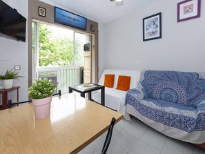 A small living area with a sofa, a table, and a TV. There is a window with a view of greenery outside. - Studio in Roses Near La Perola Beach (Roses)