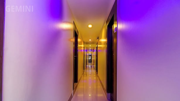 A long, narrow hallway with a reflective floor and walls, illuminated by purple lighting. - HOTEL GEMINI (Mumbai)