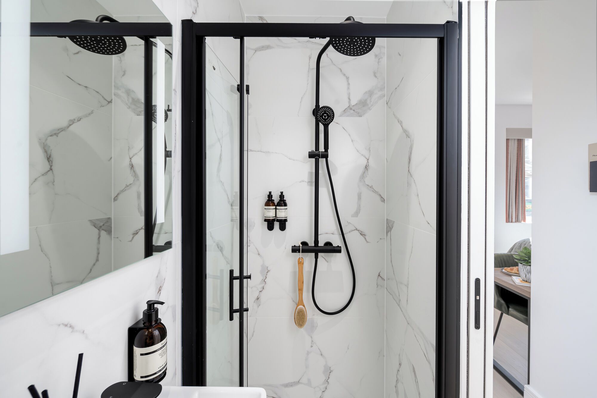 A modern bathroom with a glass-enclosed shower, marble tiles, and a visible bottle of shampoo.