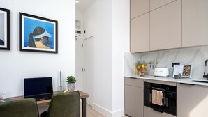 A modern kitchen with a built-in dishwasher, a toaster, and a sink. There is a dining area with a table and chairs. - Your Apartment - Camden  (London)
