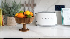 A kitchen counter with a wooden bowl of fruit, a white Smeg toaster, and a potted fern. - Your Apartment - Camden  (London)