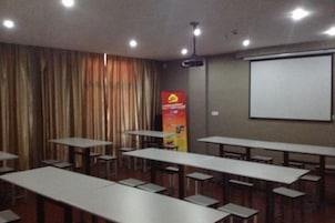 Un salón de conferencias con mesas, sillas, una pantalla de proyector y un telón de fondo.