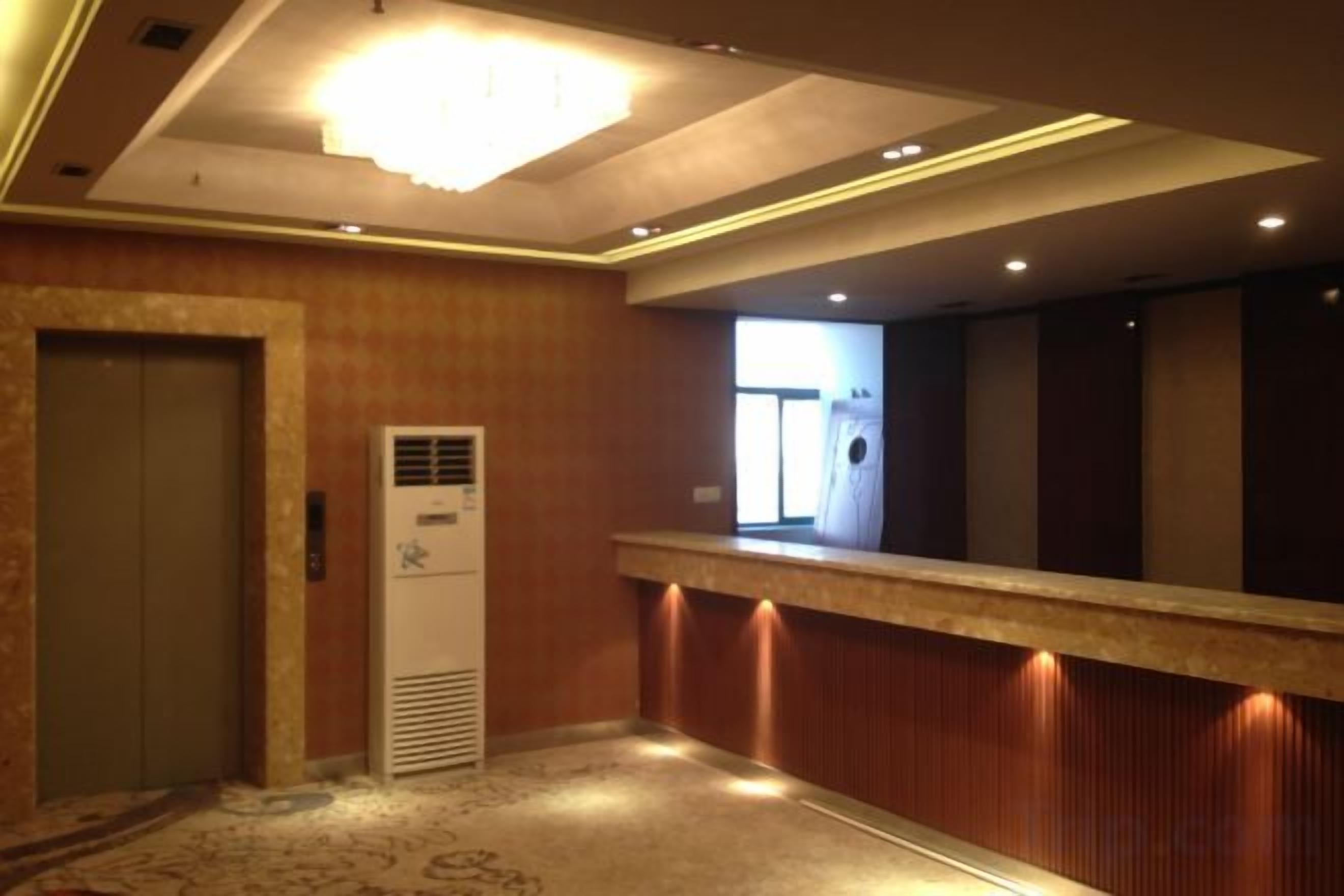 Un vestíbulo de hotel con mostrador de recepción, un ascensor y un amplio ventanal.