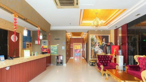 A hotel lobby with a reception desk, red and gold decor, and a chandelier.