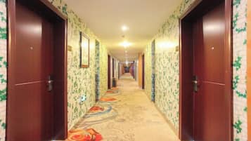 Un pasillo de hotel con pisos alfombrados, puertas de madera y papel tapiz con motivos florales.