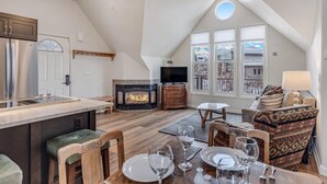 A spacious loft-style living area with a fireplace, dining table set for four, and a cozy seating area. - Victorian Under the Gondola: 1 Bedroom Apartment (Steamboat Springs)