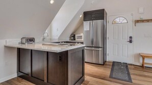 A modern kitchen with a central island, stainless steel appliances, and a sloped ceiling. - Victorian Under the Gondola: 1 Bedroom Apartment (Steamboat Springs)