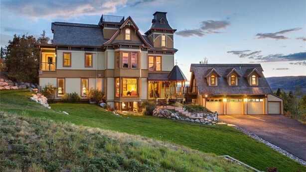 A large, two-story house with a prominent front porch, multiple windows, and a garage. - Victorian Under the Gondola: 1 Bedroom Apartment (Steamboat Springs)