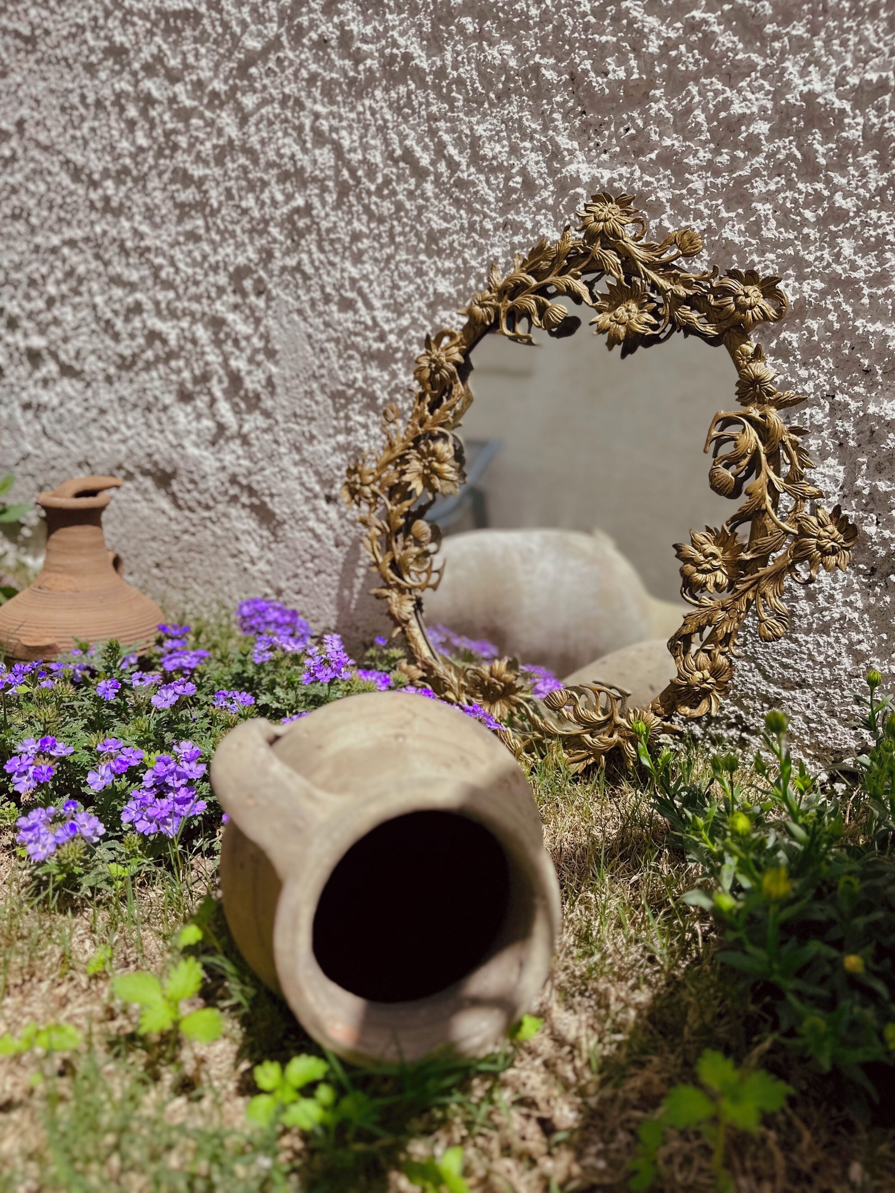 A rustic outdoor setting with a decorative mirror, a clay pot, and purple flowers.