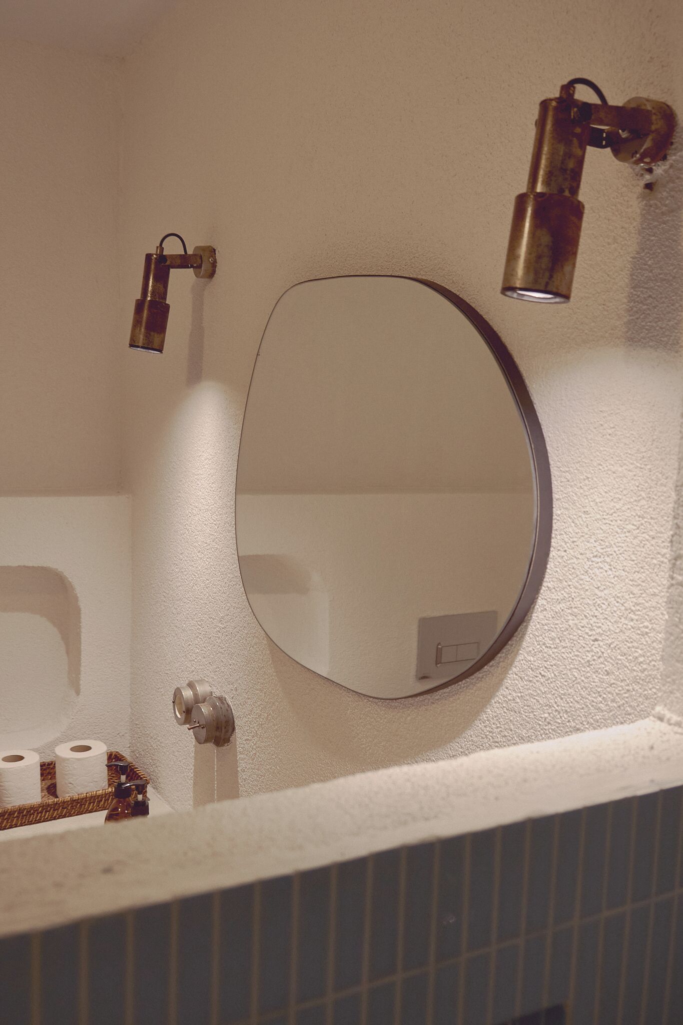 A bathroom with a round mirror, two wall-mounted lights, and a towel rack with towels.