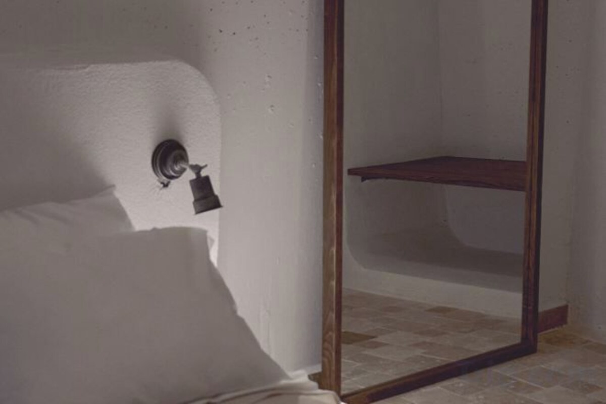 A bathroom with a white wall, a wooden door frame, and a shelf.
