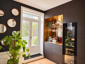 A modern interior with a dark wall, a door leading to a balcony, and a bar area with wine glasses and bottles.