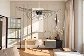 A modern bedroom with a wooden desk, a white chair, a bed, and a large window with curtains.