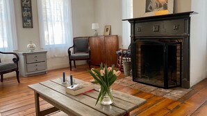 Una sala de estar acogedora con chimenea, suelo de madera, una mesa de madera con un florero y una estantería.