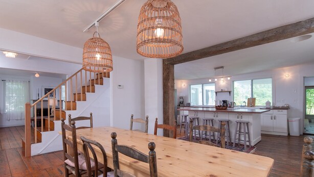 Un comedor amplio con una mesa y sillas de madera, una escalera y una cocina con taburetes de bar.