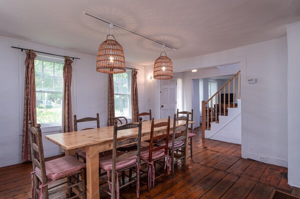 Un comedor con una mesa y sillas de madera, dos lámparas colgantes y una escalera que lleva a otra habitación.