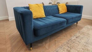 A blue sofa with yellow cushions in a room with wooden flooring and a radiator.