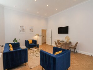 Een moderne woonkamer met blauwe banken, een glazen salontafel en een eethoek met een tafel en stoelen.