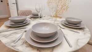 A round marble table set with grey bowls, plates, and cutlery, accompanied by a golden decorative piece and a glass. - The Salisbury Apartment 106 (Scarborough)