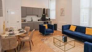 A modern living room with a blue sofa, a dining area with a round table, and a kitchen with grey cabinets. - The Salisbury Apartment 106 (Scarborough)