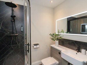 Een moderne badkamer met een douchecabine van glas, een wit toilet, een wastafel met spiegel en een potplant.