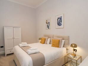 Een keurig opgemaakt slaapkamer met een bed, nachtkastjes, een kledingkast en kunst aan de muur.