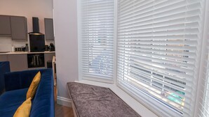 A modern living room with a blue sofa, a bench, and large windows with blinds. - The Salisbury Apartment 106 (Scarborough)