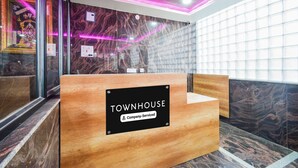 Un mostrador de recepción con la etiqueta 'TOWNHOUSE', una pared de mármol y una partición de vidrio al fondo.