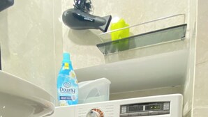 A front-loading washing machine with a control panel, a detergent bottle, and a yellow container on a shelf above it. - Lapa the Bohemian Neighborhood of Rio. The Wonderful City with Comfort and Safety. (Centro Rio de Janeiro)
