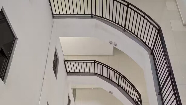 Ein mehrgeschossiges Interieur mit einer geschwungenen Treppe, weißen Wänden und kleinen Fenstern.
