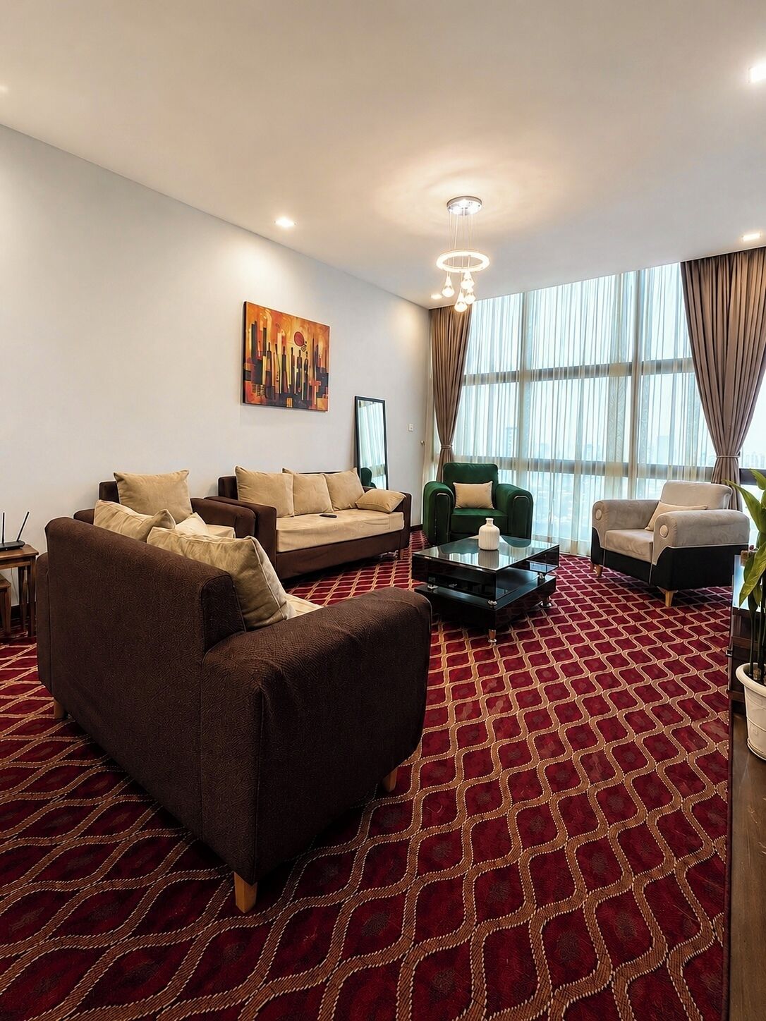 Una sala de estar moderna con una alfombra estampada, un conjunto de sofás, un sillón verde y un cuadro en la pared.