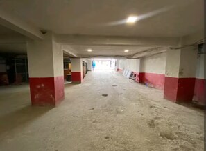 Ein langer, leerer Korridor mit Betonböden und rot-weißen Wänden, der zu einem offenen Bereich mit vereinzelten Gegenständen führt.