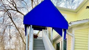 Una escalera que lleva a una casa con un toldo azul, felpudo y cielo despejado.