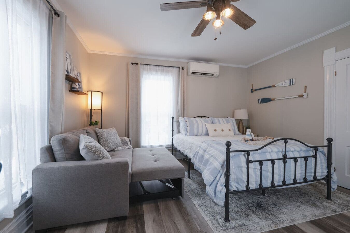 Quarto com cama, sofá, cadeira, ventoinha no teto e janela com cortinas.