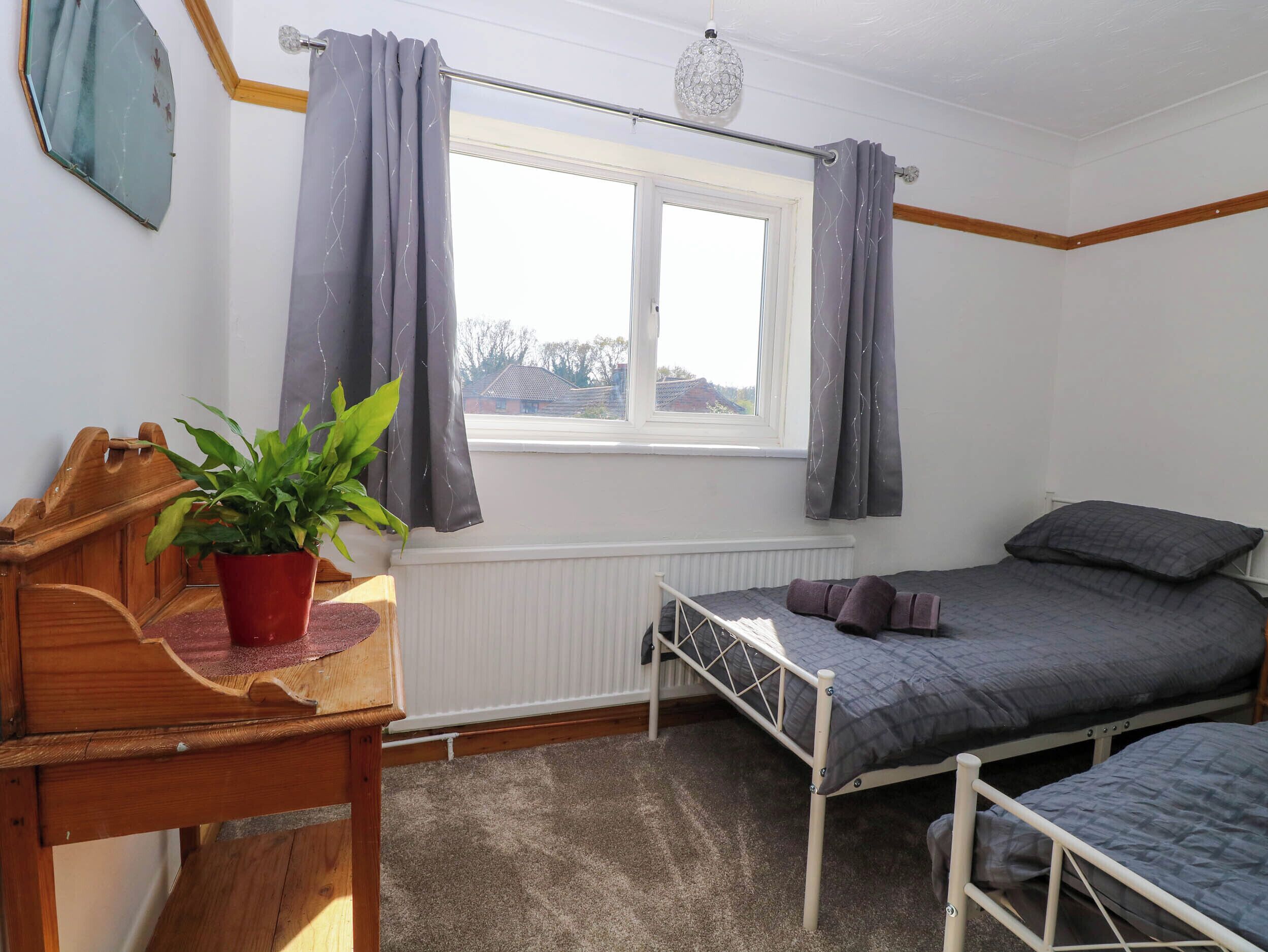 Une chambre avec deux lits, une fenêtre avec des rideaux, un radiateur, un bureau en bois et une plante en pot.