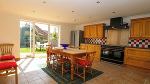 A kitchen with wooden cabinets, a black stove, and a dining area with a table and chairs. - Cedar View (Norwich)